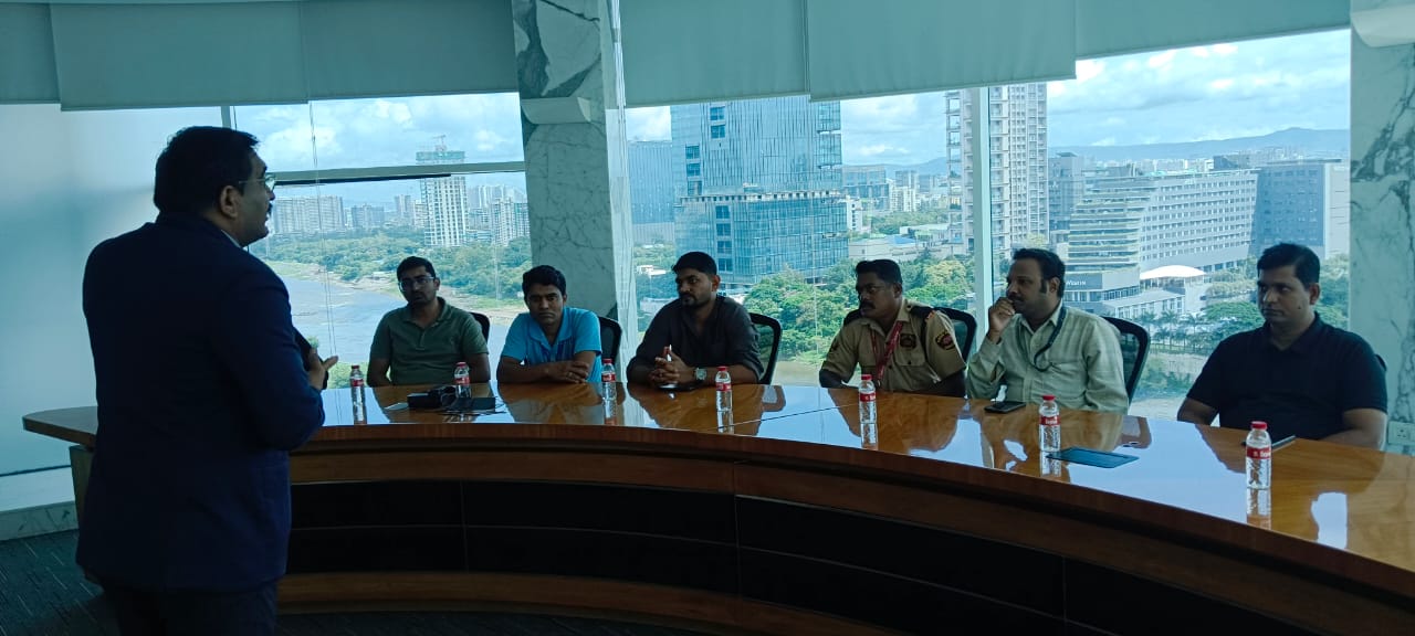 Boardroom briefing with a presenter addressing a seated group, city skyline visible through the windows