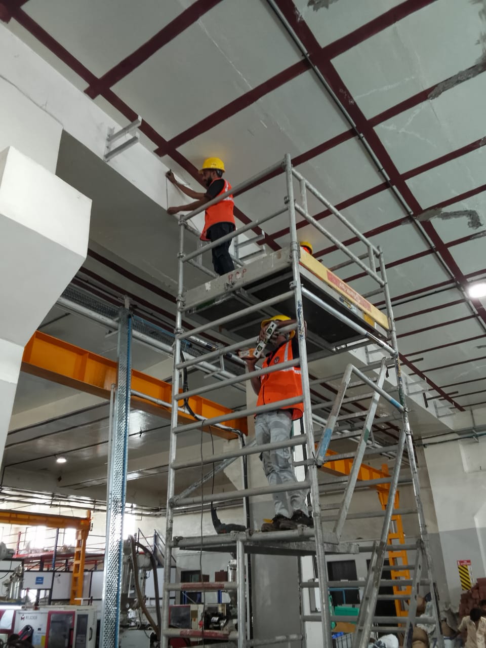 Workers on a mobile scaffold tower installing fire sprinkler piping into a ceiling grid