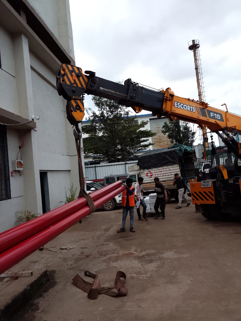 Crane lifting red-coated fire piping onto a building under construction, workers guiding it into place