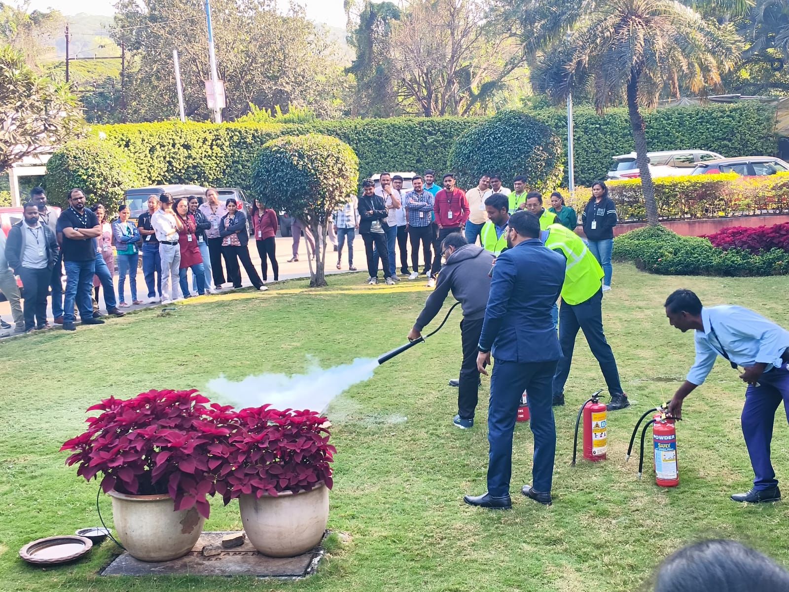 Outdoor fire extinguisher training demonstration on a lawn, staff and onlookers around the exercise
