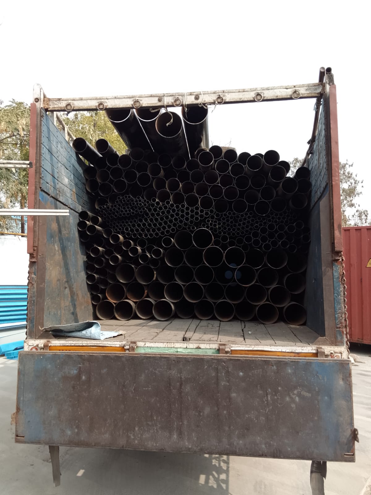 Open truck bed loaded with stacked black steel pipes for site delivery