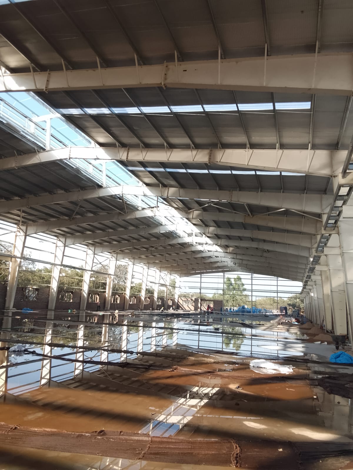 Large industrial shed under construction with a flooded concrete floor reflecting the roof structure